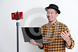 Adult Asian man holding a laptop while talking during online meeting using mobile phone photo