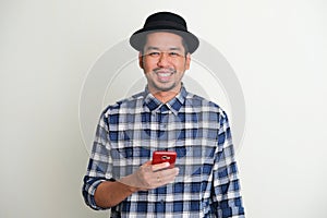 Adult Asian man looking to the camera when holding mobile phone and showing happy expression