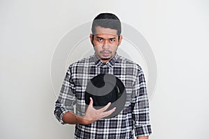 Adult Asian man put his hat on chest and showing sad expression when looking to camera photo