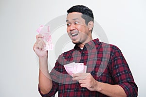 Adult Asian man showing amazed expression when looking to money that he hold