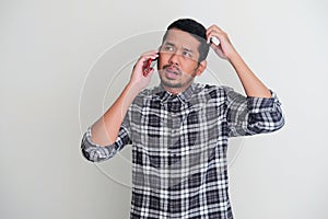Adult Asian man showing confused expression while talking with someone on the phone photo