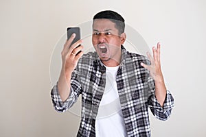 Adult Asian man showing rage expression when looking to his cellular phone photo