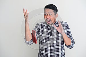 Adult Asian man showing shocked face expression when mobile phone fall from his hand photo