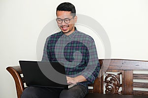 Adult Asian man sitting in a bench while working using his laptop photo