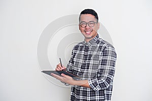 Adult Asian man smiling confident while working using his mobile tablet gadget photo