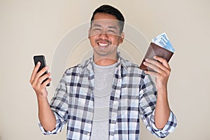 Adult Asian man smiling happy while holding mobile phone and showing paper money from his wallet