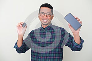 Adult Asian man smiling happy while showing blank mobile phone screen and holding a car key