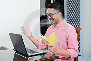 Adult Asian man smiling while in online meeting using laptop photo