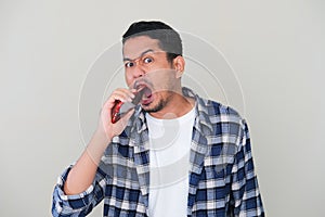 Adult Asian man trying to eat his mobile phone