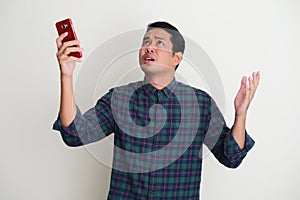 Adult Asian man trying to search his mobile phone signal connection with worried expression photo