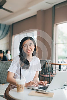 Adult asian woman in white shirt sitting at table with laptop