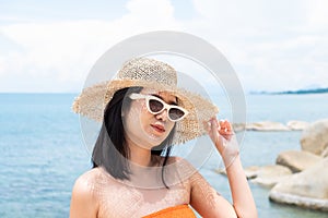 Adult Asian women wearing sunglasses and straw hat smile and feeling happy at the beach. Tropical travel lifestyle with sea,