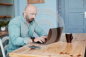 An adult attractive man works at the computer during morning coffee. Businessman typing on a laptop during Breakfast. Business,