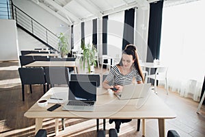 Adult attractive woman on her work is holding phone and sitting with a laptop. Beautiful female multitasking.