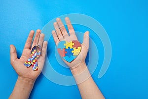 Adult and autistic boy hands holding puzzle heart shape and ribbon. Autism spectrum disorder family support concept