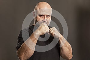 Adult bald man in a fighting stance. Gray background