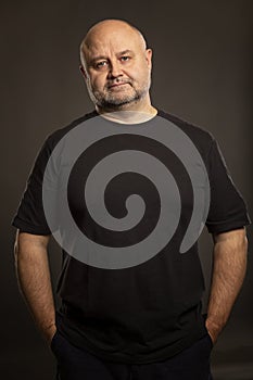 Adult bald man is standing, portrait on dark background