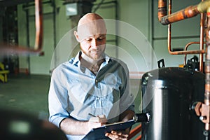 Adult bald smiling attractive man forty years with beard in blue shirt businessman. Engineer near the control cabinet of