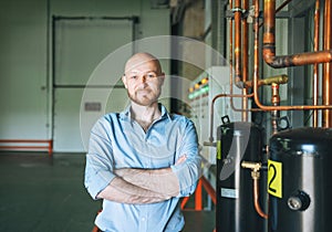 Adult bald smiling attractive man forty years with beard in blue shirt businessman. Engineer near the control cabinet of