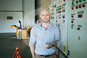 Adult bald smiling attractive man forty years with beard in blue shirt businessman. Engineer near the control cabinet of