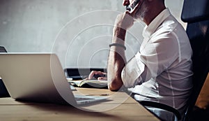 Adult bearded businessman wearing classic glasses and working at the wood table in modern loft.Horizontal closeup