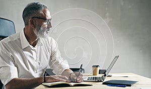 Adult bearded businessman working on mobile laptop computer while sitting at wooden table.