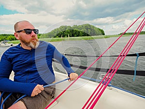 Adult bearded man using a winch to pull a blue rope on a sailboat or sailing yacht