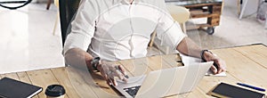 Adult bearded man working on mobile laptop computer while sitting at wooden table.Cropped. Wide.