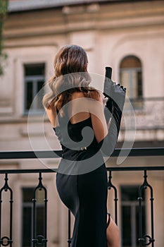 An adult beautiful girl in an elegant black dress. A Young woman holding a gun