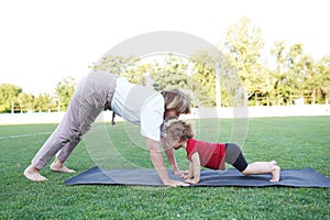 Adult beautiful woman and little girl are doing yoga exercises at park with beautiful nature outside