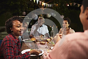 Adult black family eat dinner in garden, over shoulder view