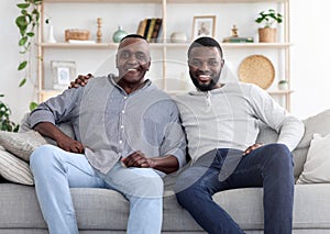 Adult black son and his senior father posing on couch at home