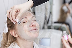 Adult blonde woman apply face cream in a beauty salon. Close-up. Age-related beauty treatments