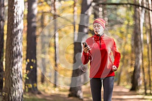 Adult breathless woman in red sportswear jogging outdoor with cellphone and wired headphones as a music player in the photo