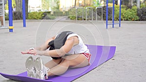 Adult brunette caucasian woman stretching the leg on a purple karemat at warm sunny day