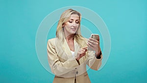 Adult business lady with blond hair using smartphone scrolling web pages and chatting in social network zooming  surprised face