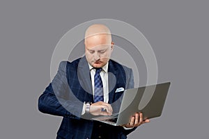 An adult businessman with a laptop in his hand looks at a wristwatch.