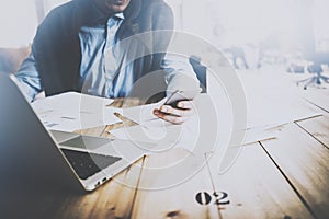 Adult businessman working at office on laptop while sitting at the wooden table.Man looking at the smartphone in his