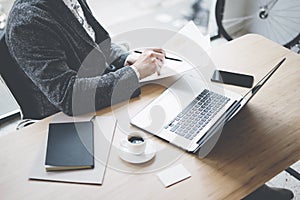 Adult businessman working at sunny office on laptop while sitting at the wooden table.Man analyze document in his hands