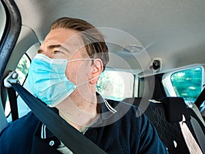 Adult caucasian 40s male passenger of a car moving wearing surgical 3 ply protection face mask, daylight, sunny