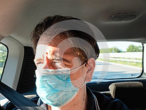Adult caucasian 40s male passenger of a car moving wearing surgical 3 ply protection face mask, daylight, sunny