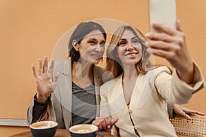 Adult caucasian business women sit with phones during break in street cafe and take selfie.