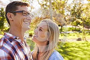 Adult Caucasian couple embracing in a park looking away