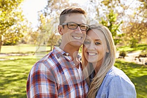 Adult Caucasian couple embracing in a park looking to camera