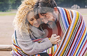 Adult caucasian couple enjoy love and relationship using together a smart phone device and having fun covered with colorful knit