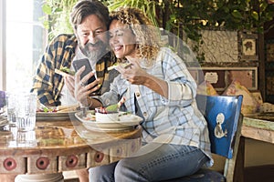 Adult caucasian couple man and woman in video conference call on mobile phone during lunch at cafe restaurant together. Cheerful