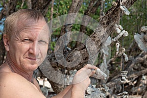 Adult Caucasian man close-up on a tropical island tying corals to a tree. Make a wish.