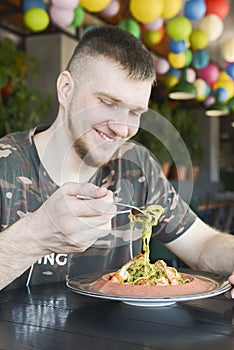 Adult caucasian man at a restaurant eating spinach pasta with shrimps. Traditional Italian cuisine, eating out concept