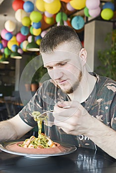 Adult caucasian man at a restaurant eating spinach pasta with shrimps. Traditional Italian cuisine, eating out concept