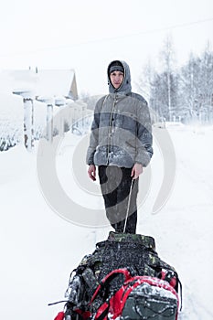 Adult Caucasian man walking with drag sled in the snowy village during strong snowfall and cold weather